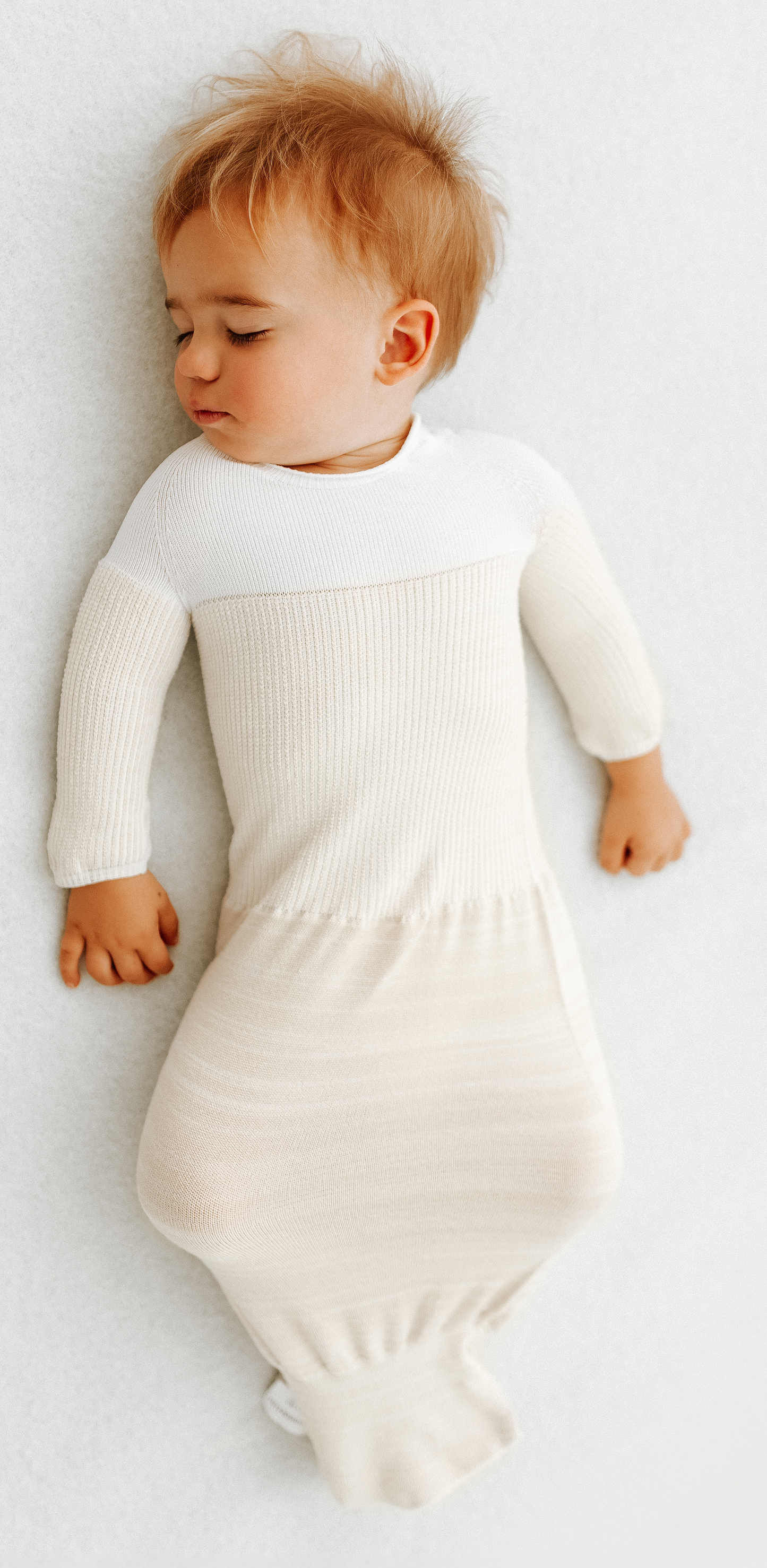 An older baby sleeping in an arms out swaddle.