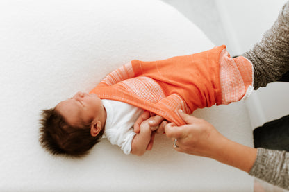 A mother putting her infant into a stretchy swaddle.