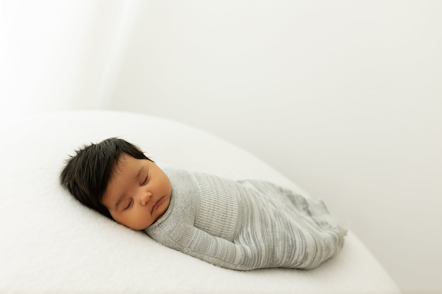 A sleeping infant in a grey sleep sack.