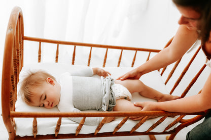 A mother changing her toddler's diaper in a bassinet.