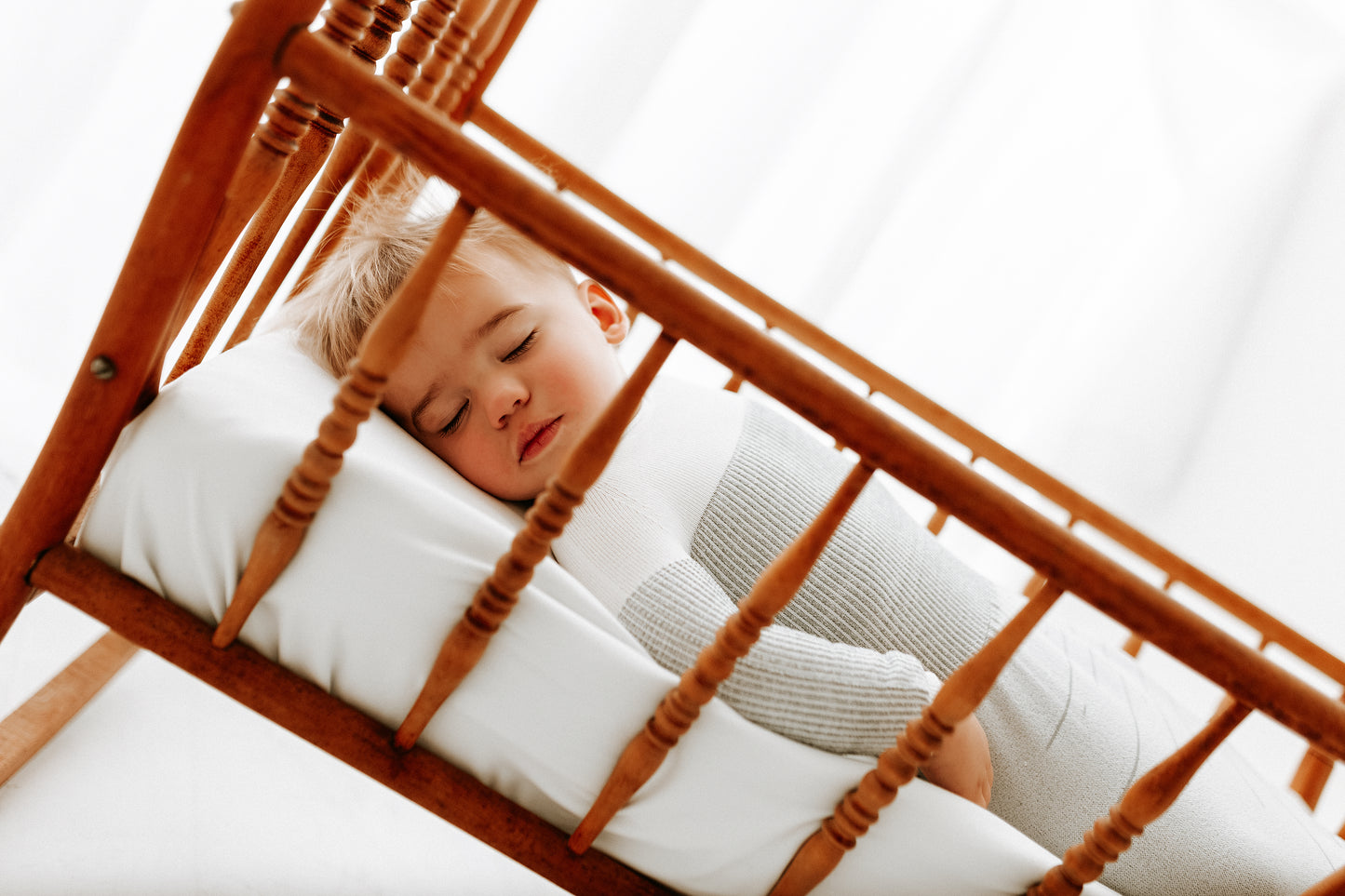 A baby resting in a bassinet with a sleep sack on.