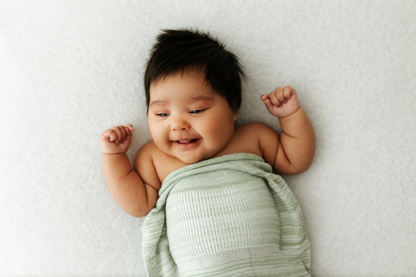 A baby with its arms out of its swaddle.