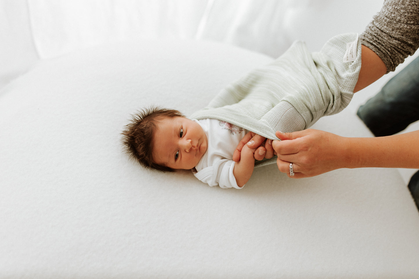 A mother putting her baby in an infant swaddle.