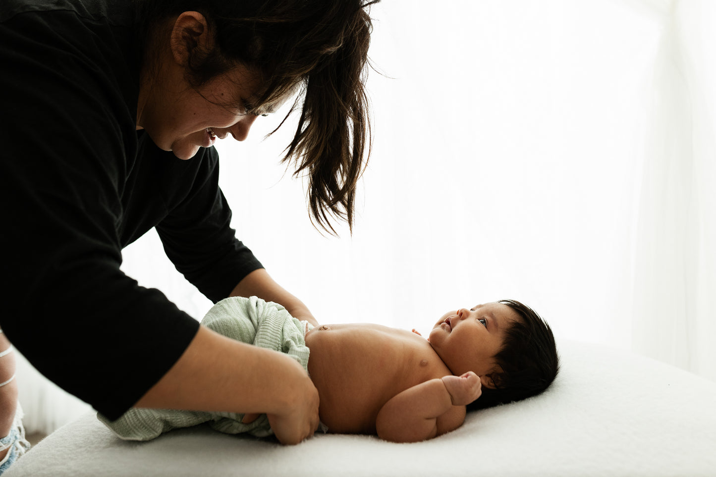 A mother putting a mint colored sleep sack on her tired baby.