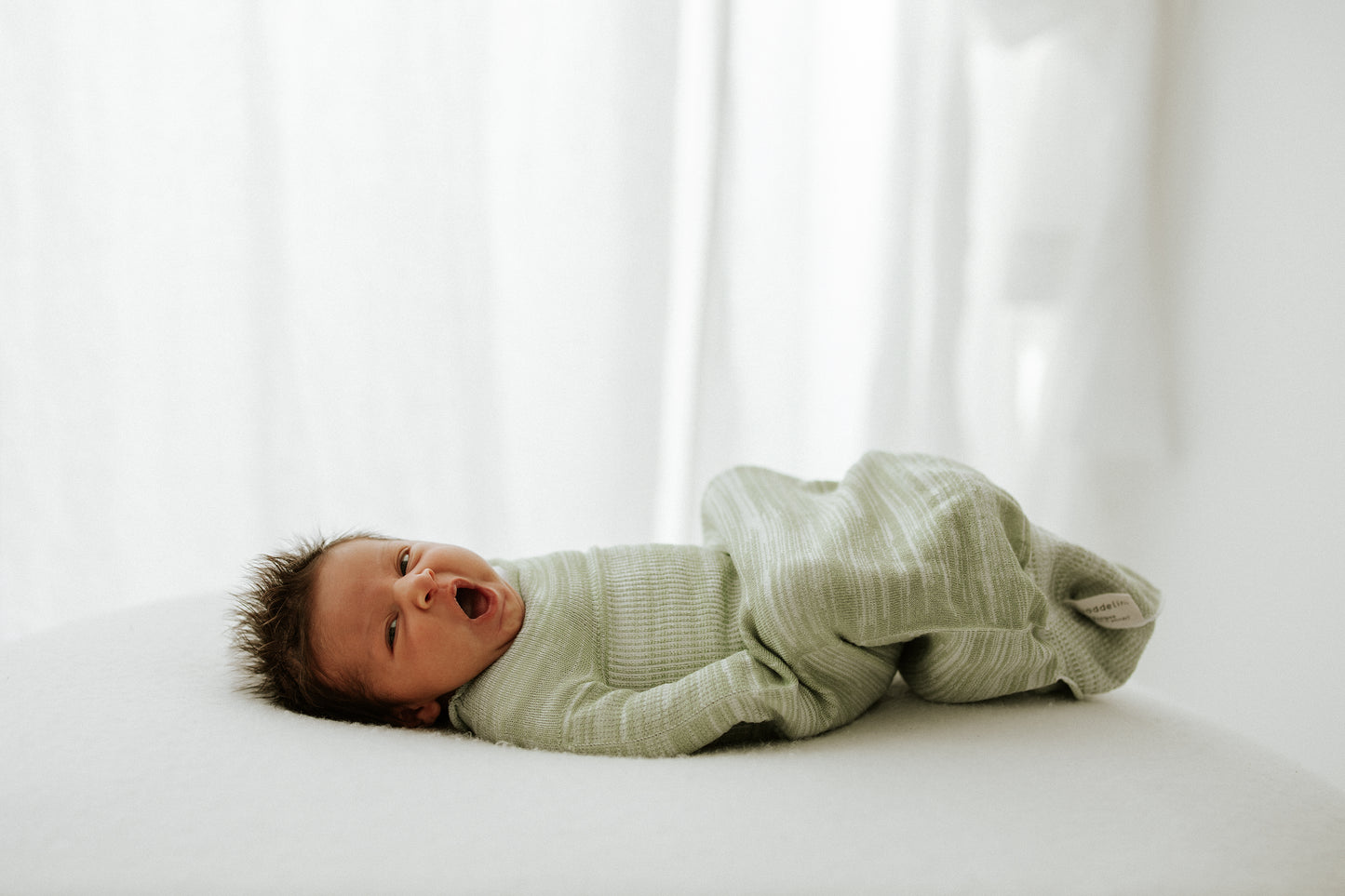 An infant in a mint colored sleep sack.