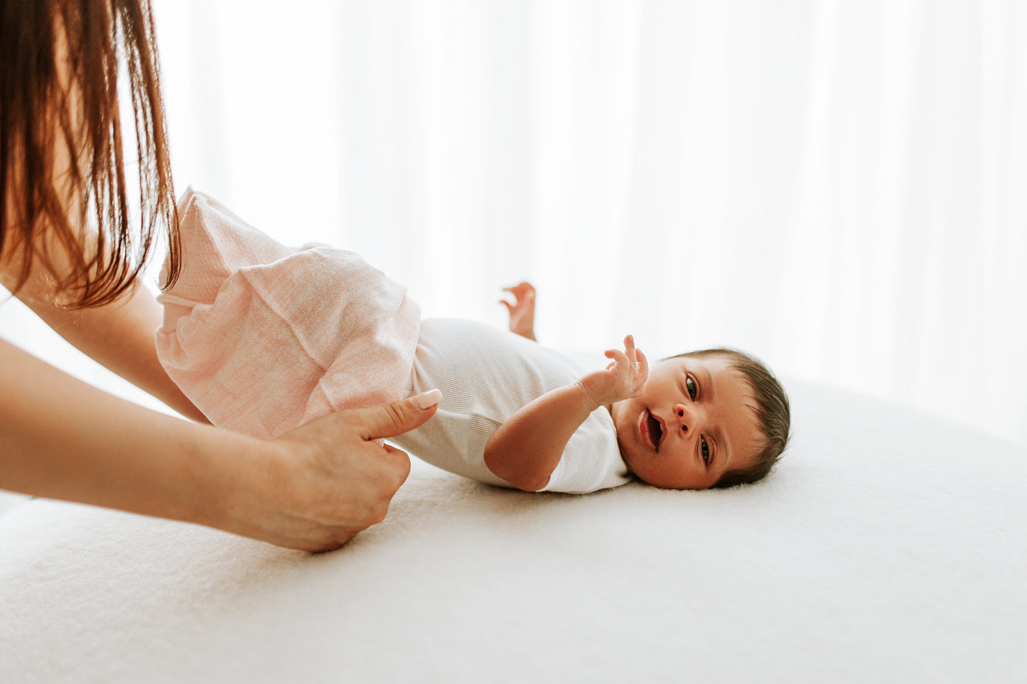 A mother putting her baby into a pink sleep sack.