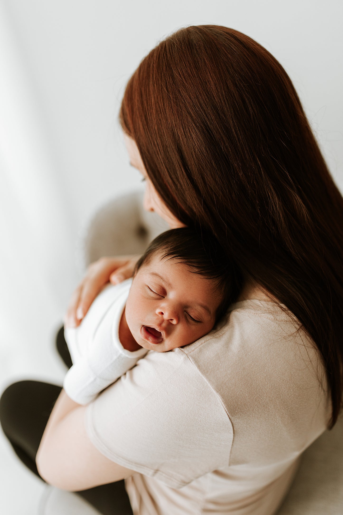 A baby sleeping on her mother's shoulder while in a swaddle.