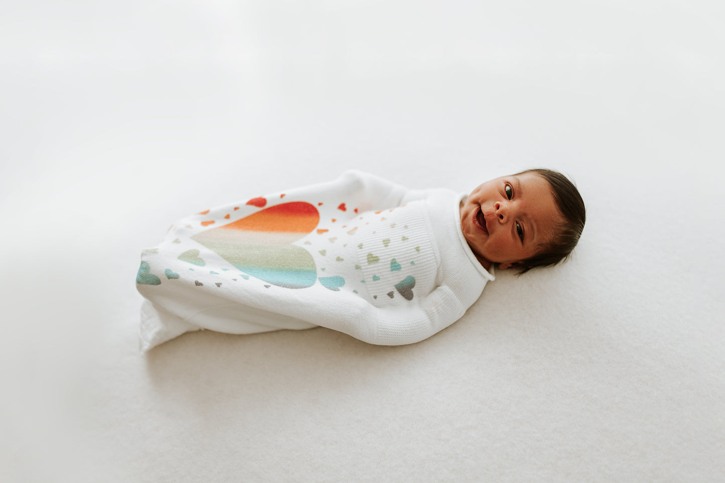 A happy baby in a rainbow swaddle.