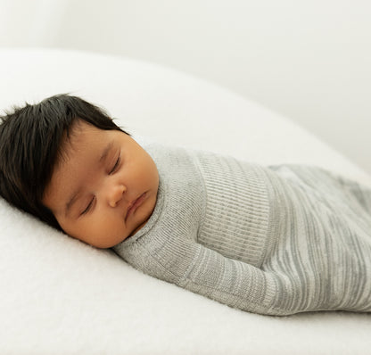 An infant sleeping in a grey baby swaddle.