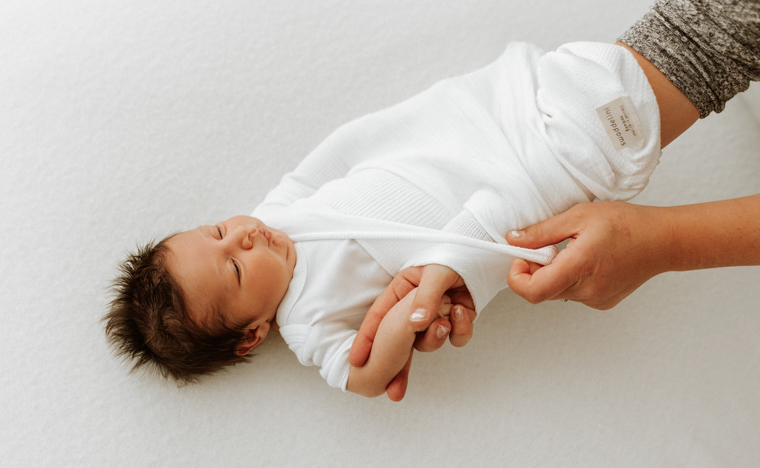 A baby being put into a knitted sleep sack.