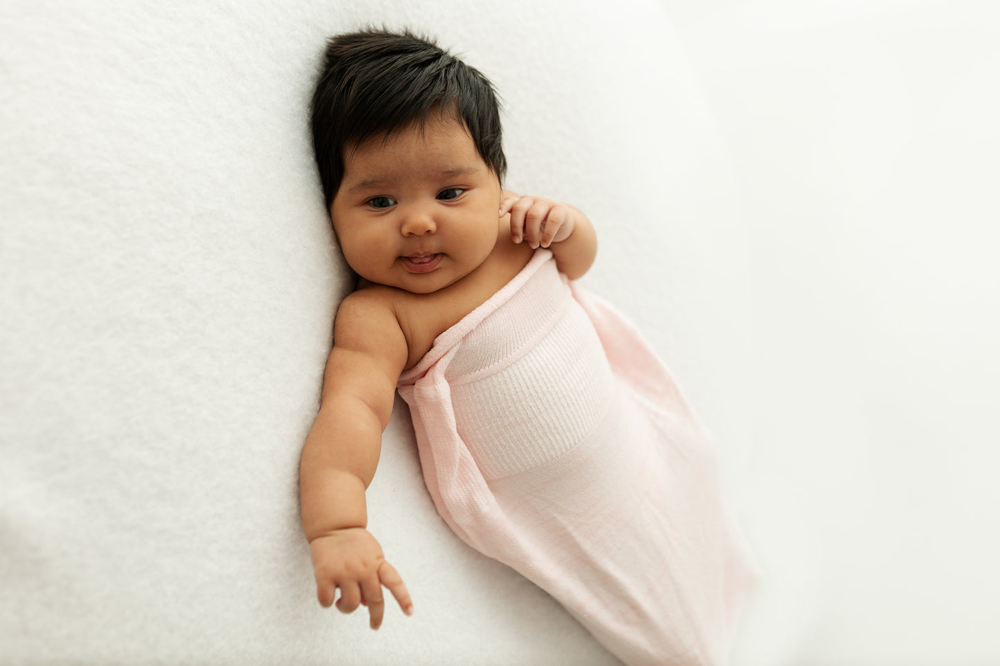 A baby lying with its arms out of its swaddle.