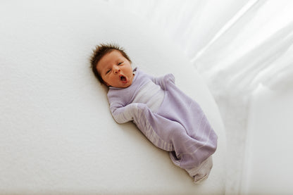 A tired baby lying in a bamboo sleep sack.