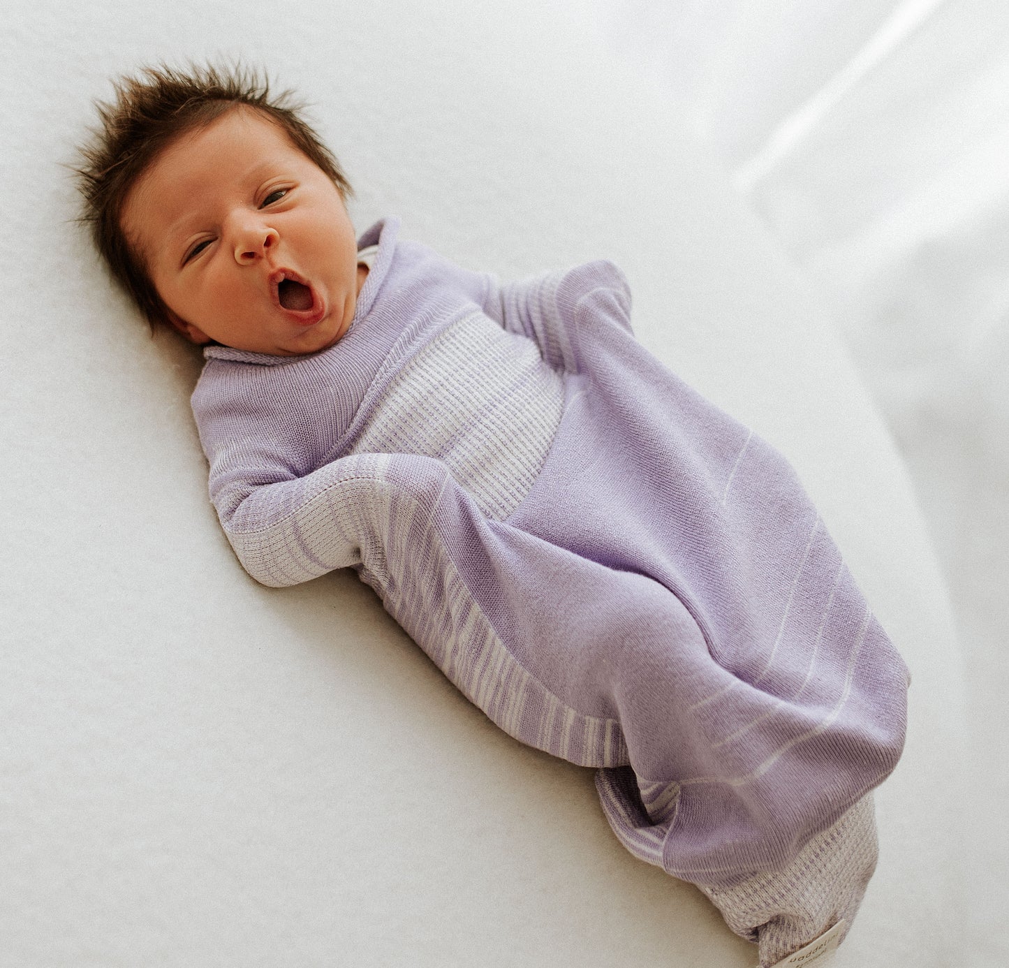 A yawning baby in a lavender sleep sack.