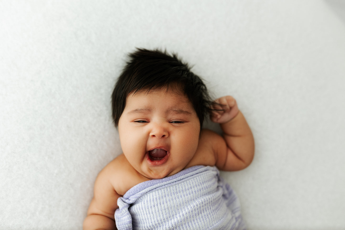 A baby lying in a bamboo swaddle with its arms out.