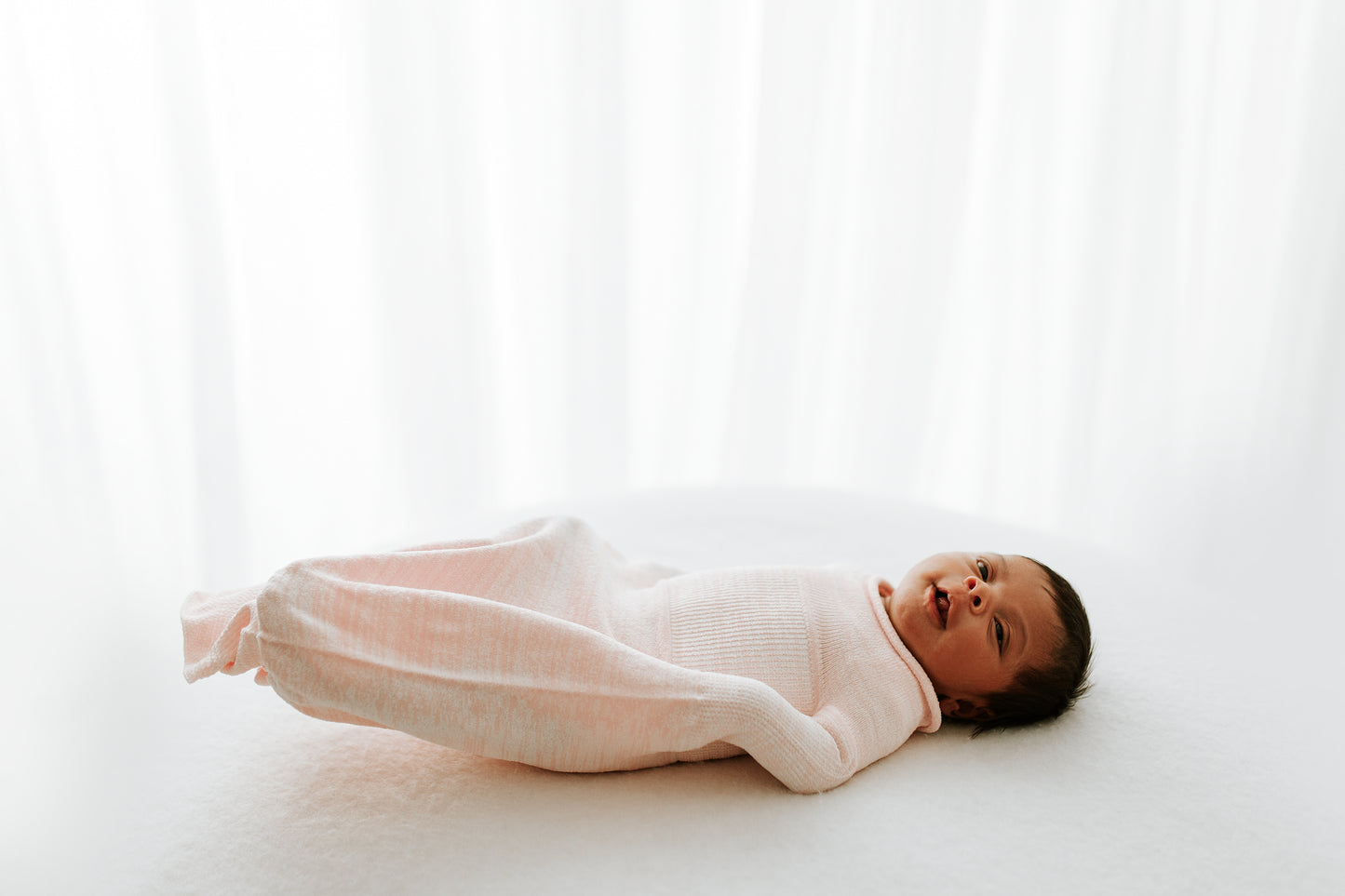 A baby lying in a pink swaddle.