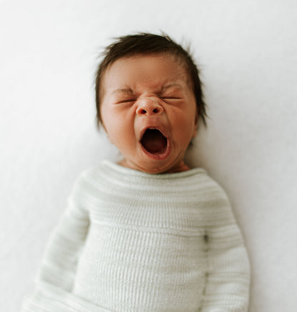 A yawning infant in an infant sleep sack.
