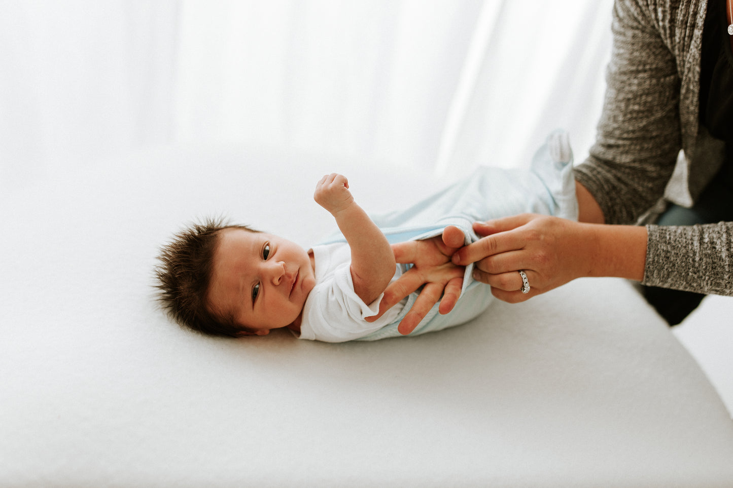 A mother putting a blue sleep sack on her infant.