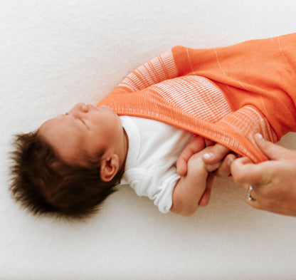 A baby being put into an orange infant swaddle.